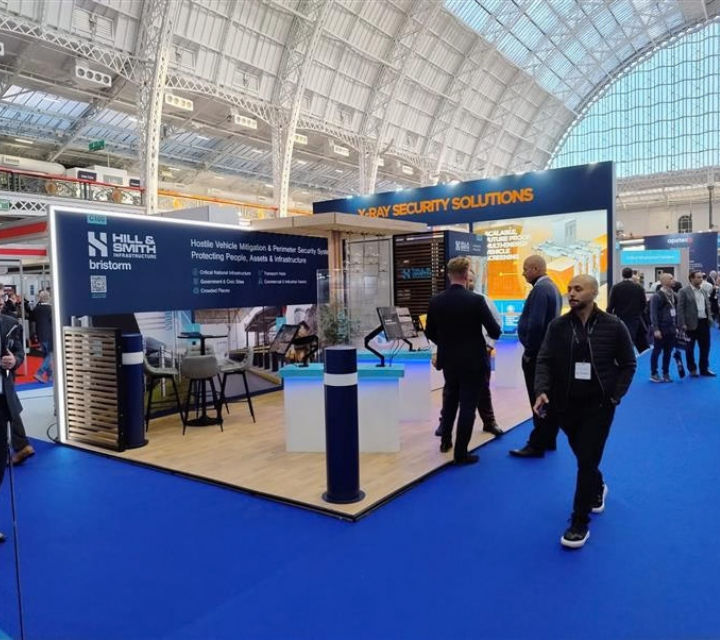 Eventa's exhibition stand for Hill & Smith Infrastructure in a glass-roofed hall, with touchscreen podiums and visitors.